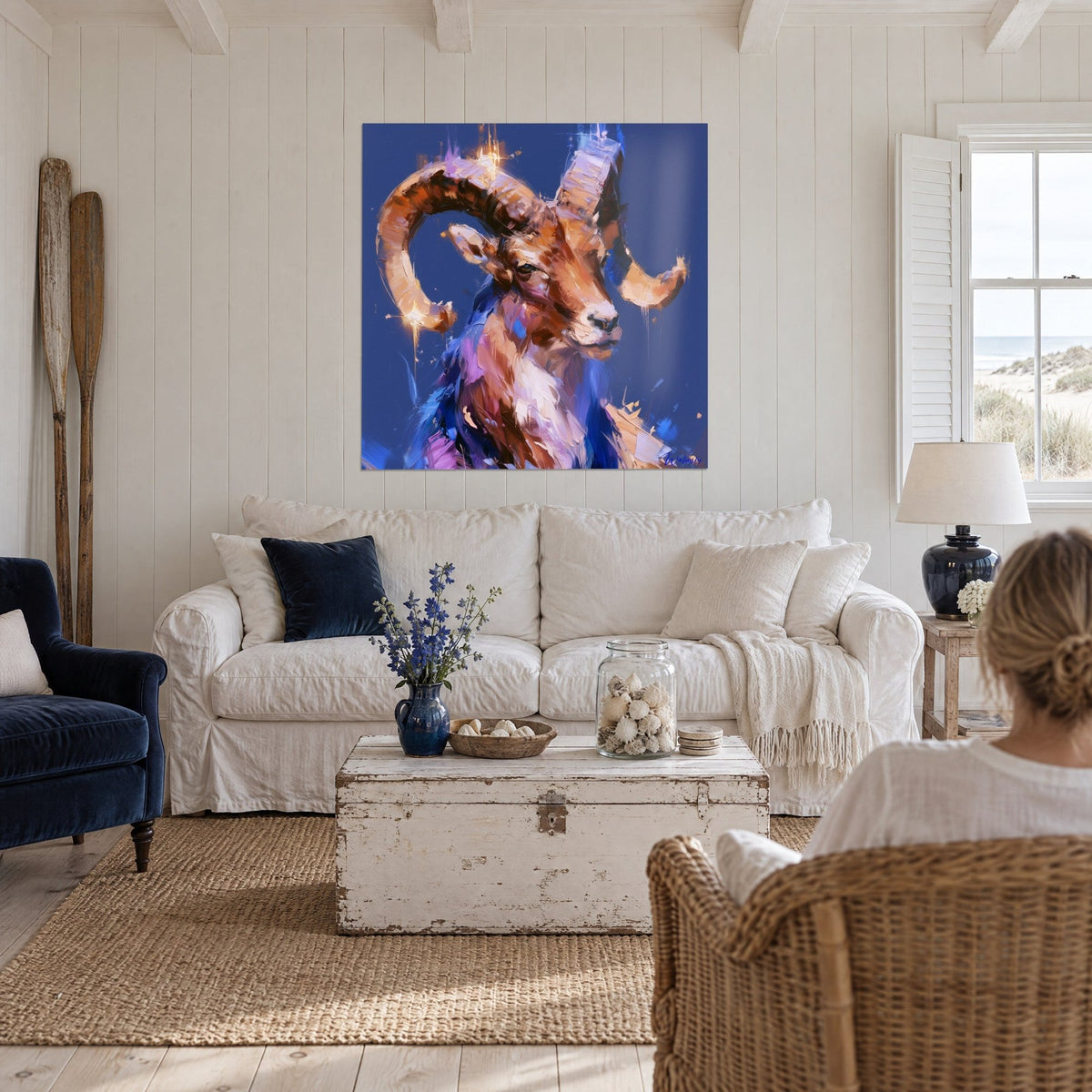 Quadro ariete con corna fulve a spirale su fondo blu navy, tocchi rosa e lilla, sopra un divano in un soggiorno luminoso
