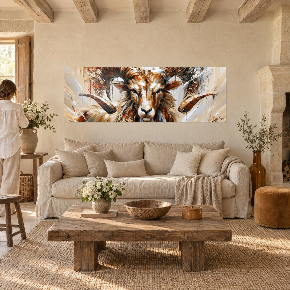 Tableau bélier aux grandes cornes en spirale cuivrées, pelage fauve et beige, une personne de dos, au-dessus d'un canapé dans un salon lumineux