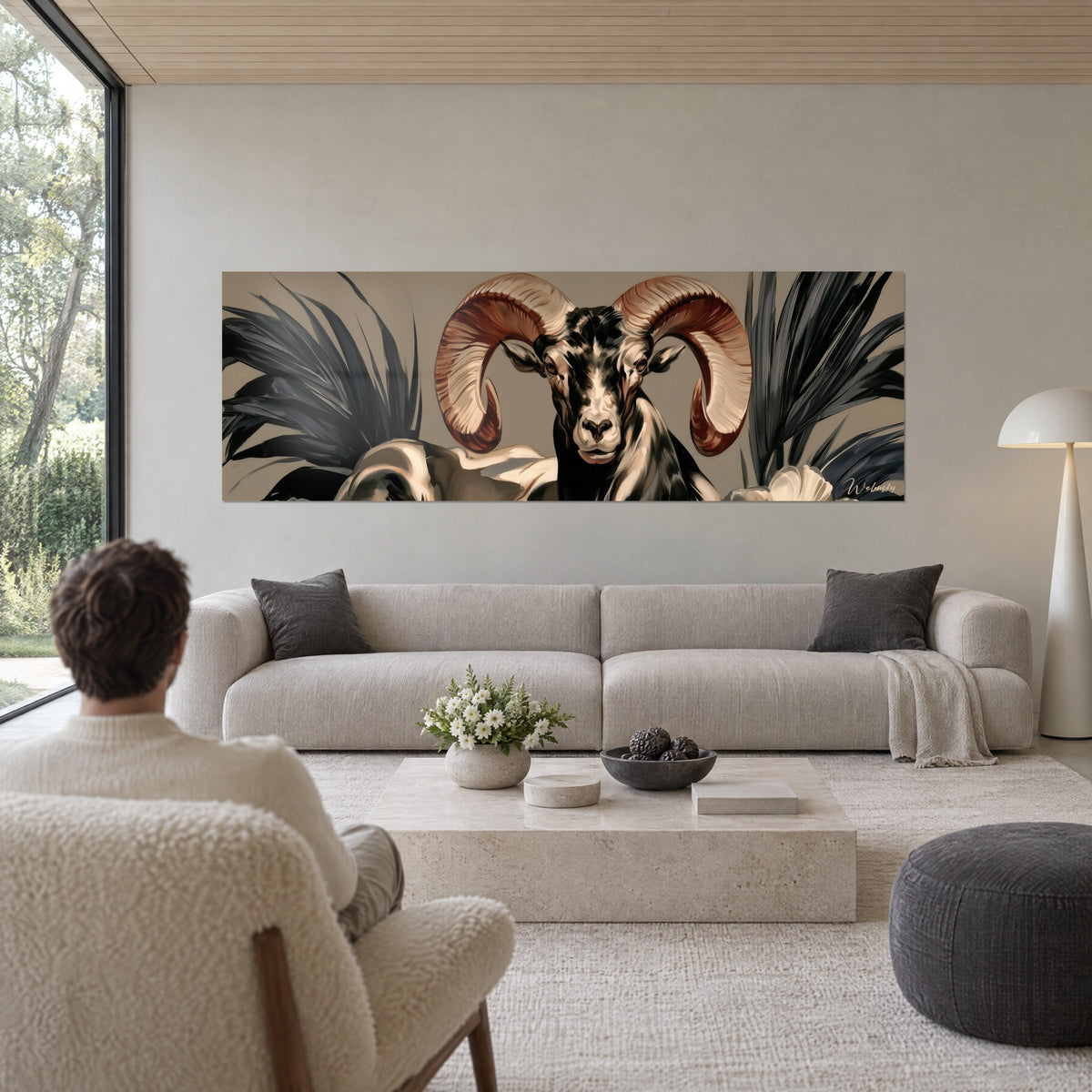 Tableau bélier aux cornes spiralées terracotta, palmes anthracite sur fond taupe, au-dessus d'un canapé dans un salon lumineux