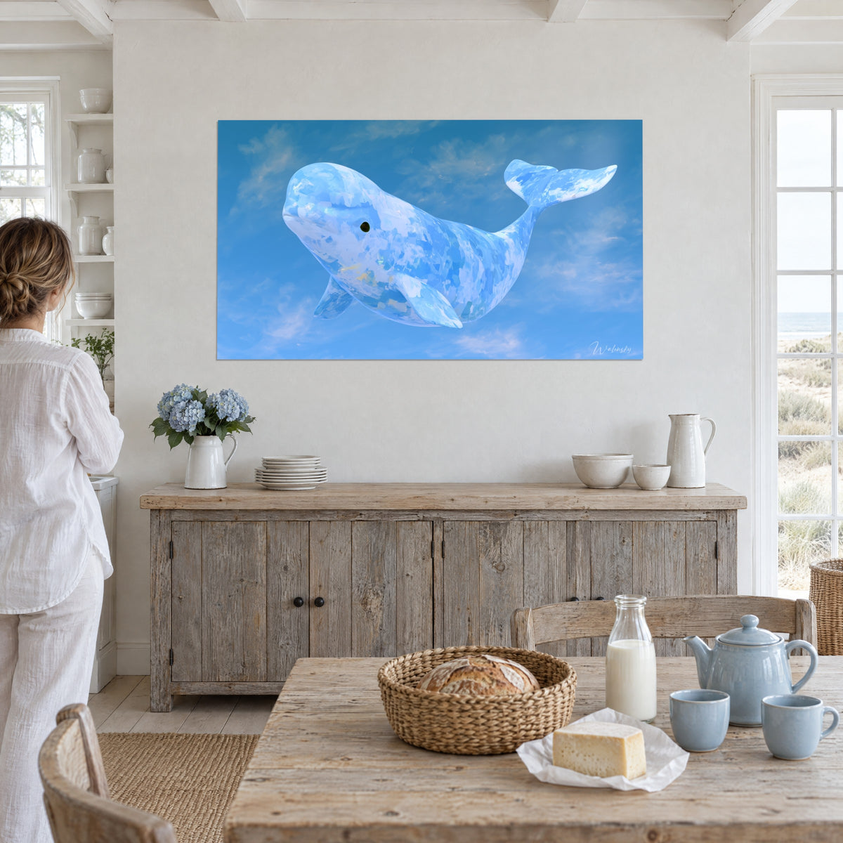 Tableau grand béluga en aplats cobalt et blanc crème, nageoire dressée dans un ciel dégradé, au mur d'une salle à manger près d'une femme en tunique blanche