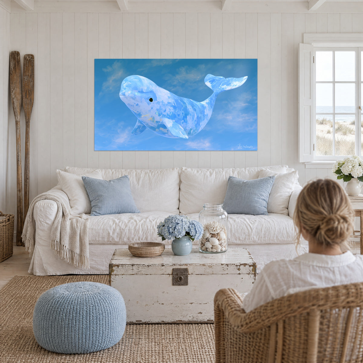 Tableau béluga bleu ciel aux écailles de peinture nacrées, volant parmi des nuages blancs, au-dessus d'un canapé dans un salon lumineux