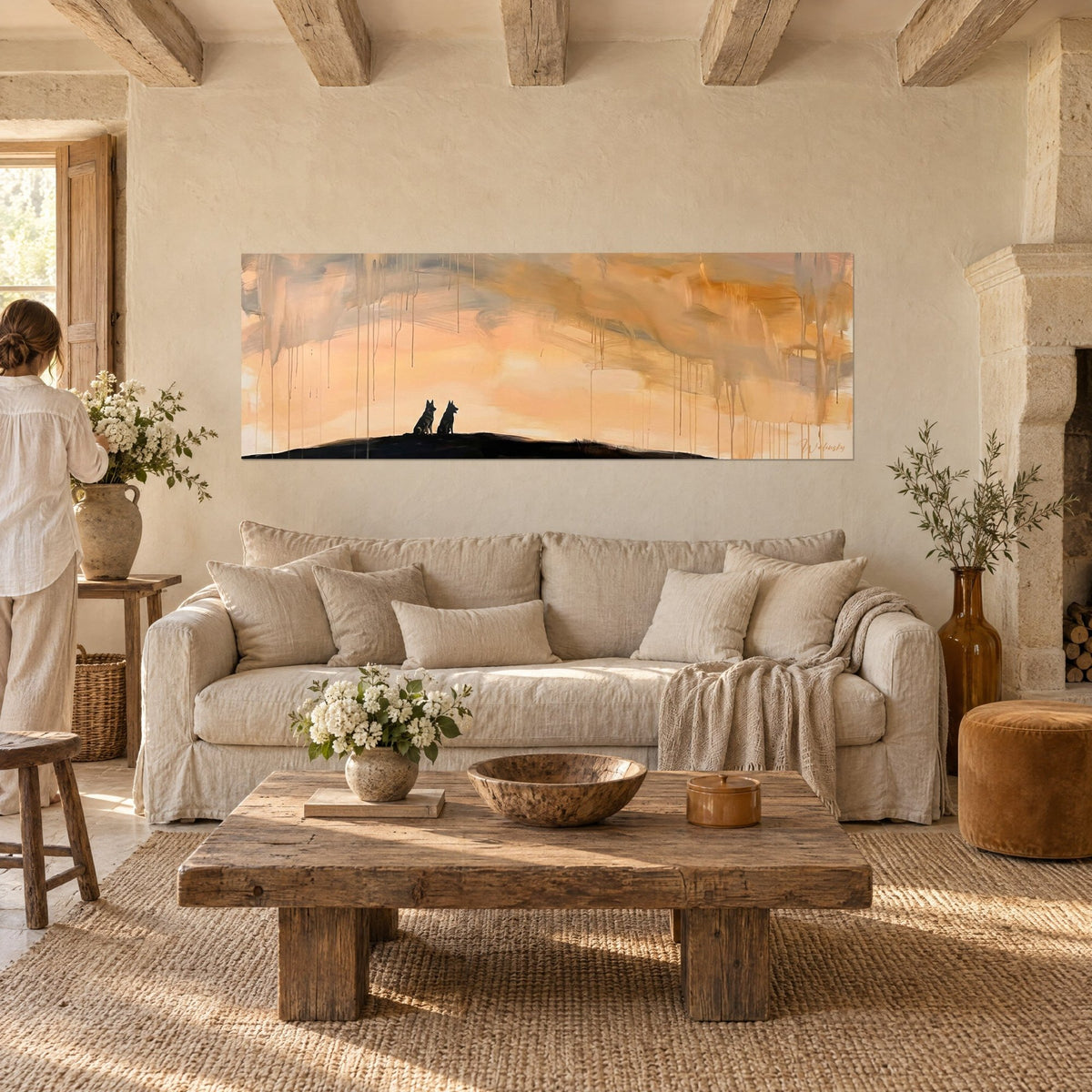 Wall art two German shepherds in silhouette on a hill, peach and ochre sky streaked with drips, above a sofa in a bright living room