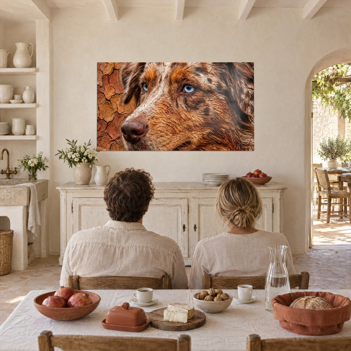 Tableau visage de chien aux yeux bleus perçants, poils bruns et terre rouge fendillée, face à un couple attablé dans une cuisine de mas