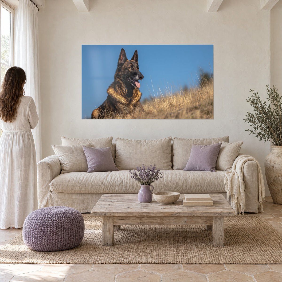 Wall art brindle Belgian Shepherd with pink tongue, tawny and black coat against a blue sky, a woman seen from behind above a sofa in a bright living room