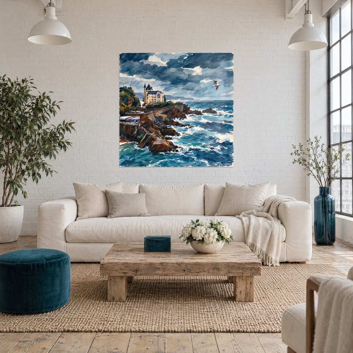 Gemälde Villa mit schieferfarbenen Türmchen auf brauner Klippe, anthrazitblaues Meer mit weißer Gischt, über einem Sofa in einem hellen Wohnzimmer