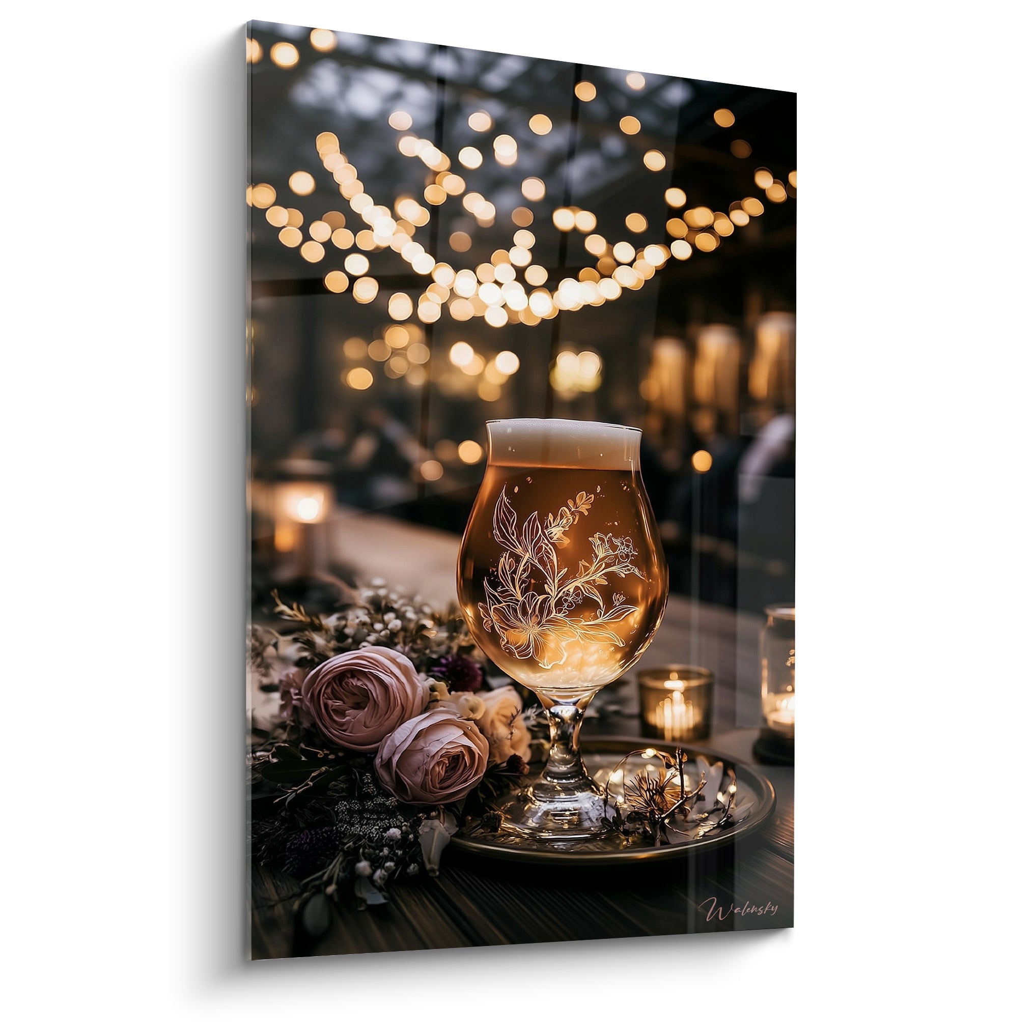 Verre de bière ambrée gravé de fleurs blanches, entouré de roses roses et bougies dorées