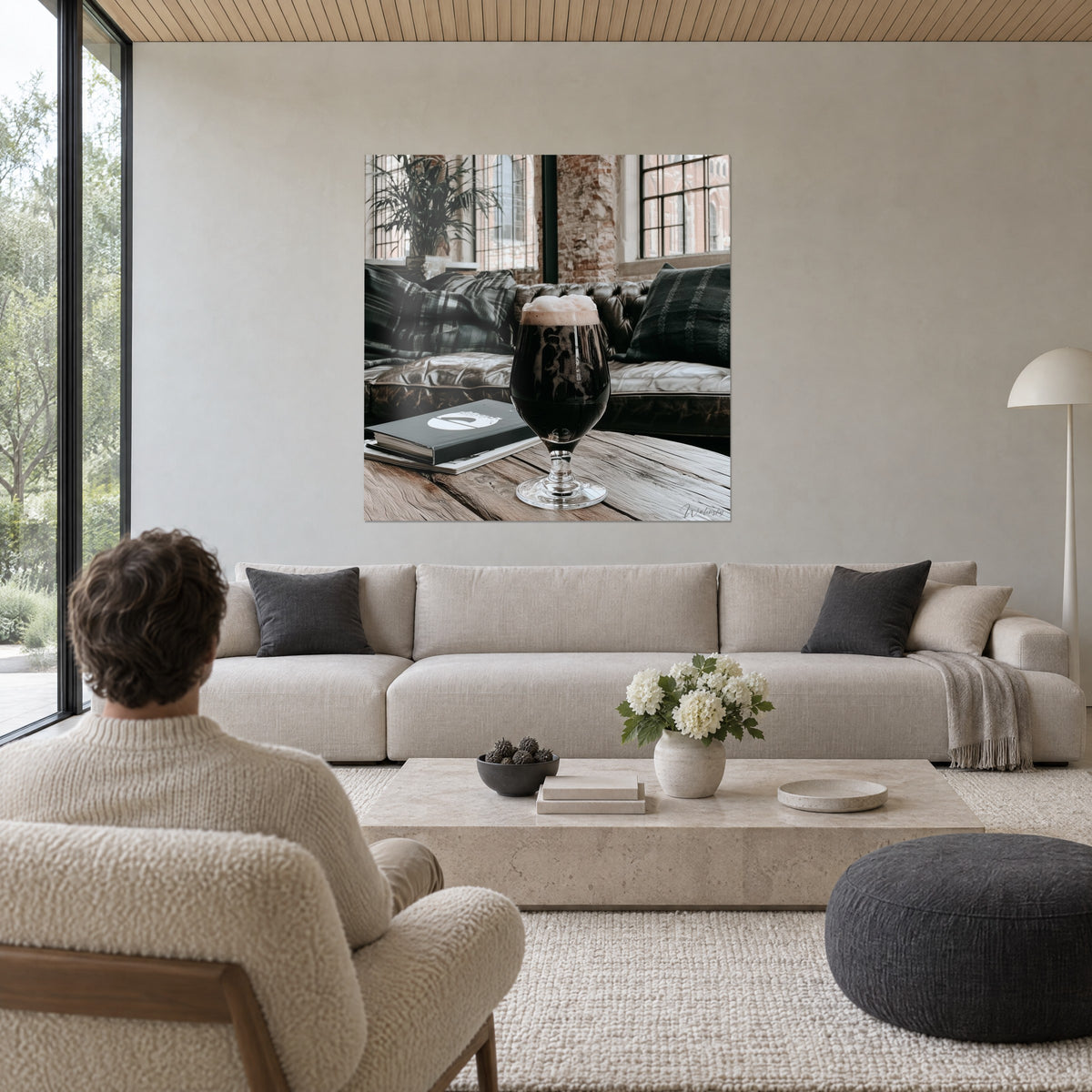 Schilderij donkerbruine stout-mok met romig schuim, bruine lederen Chesterfield-bank en grijze geruite plaid, boven een bank in een lichte woonkamer