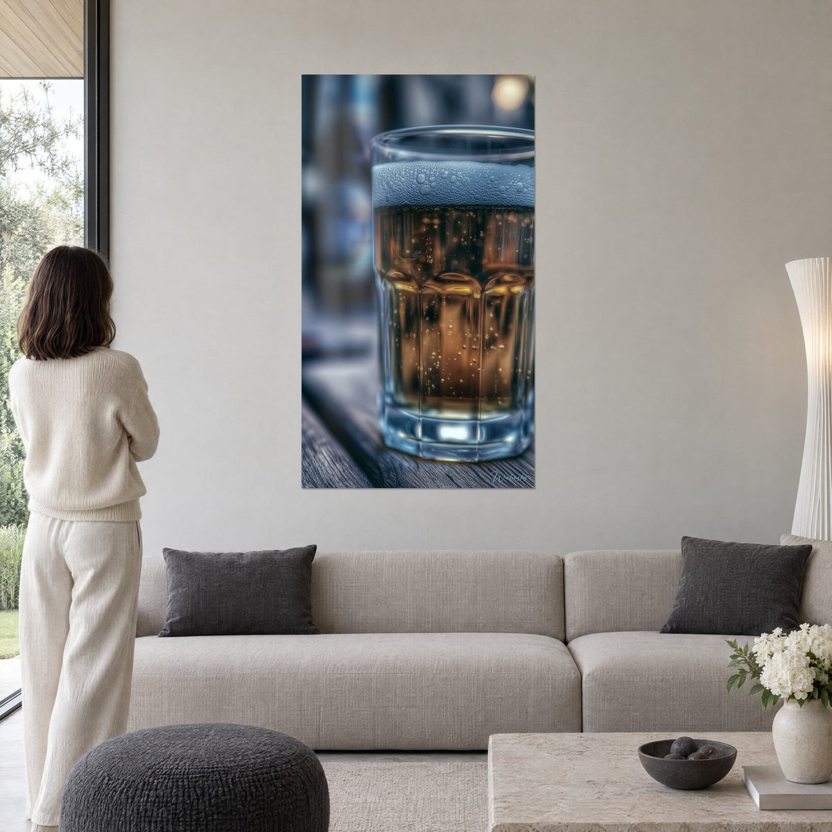 Wall art beer in a faceted glass, bluish foam and amber liquid, woman seen from behind, above a sofa in a bright living room