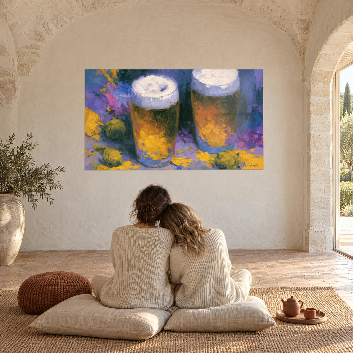 Schilderij duo van amberkleurig bier met witte romige kop, gele accenten en ultramarijnblauw, koppel met de rug naar de kijker op kussens op de vloer