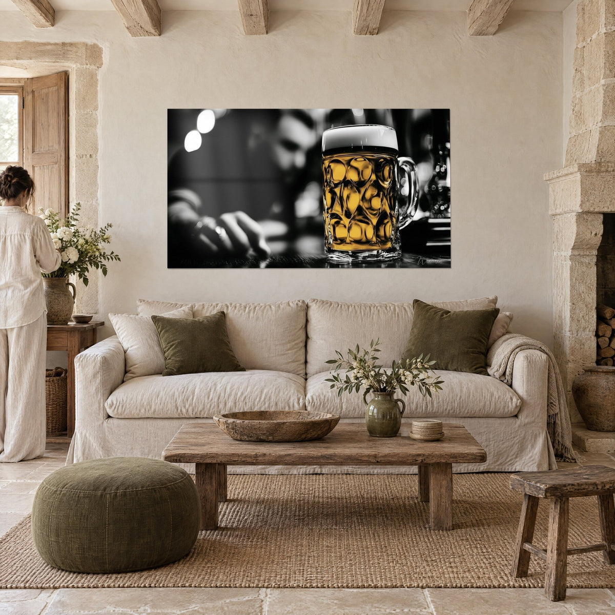 Tableau chope de bière dorée au verre facetté, mousse blanche et fond noir flou, femme de dos au-dessus d'un canapé dans un salon lumineux