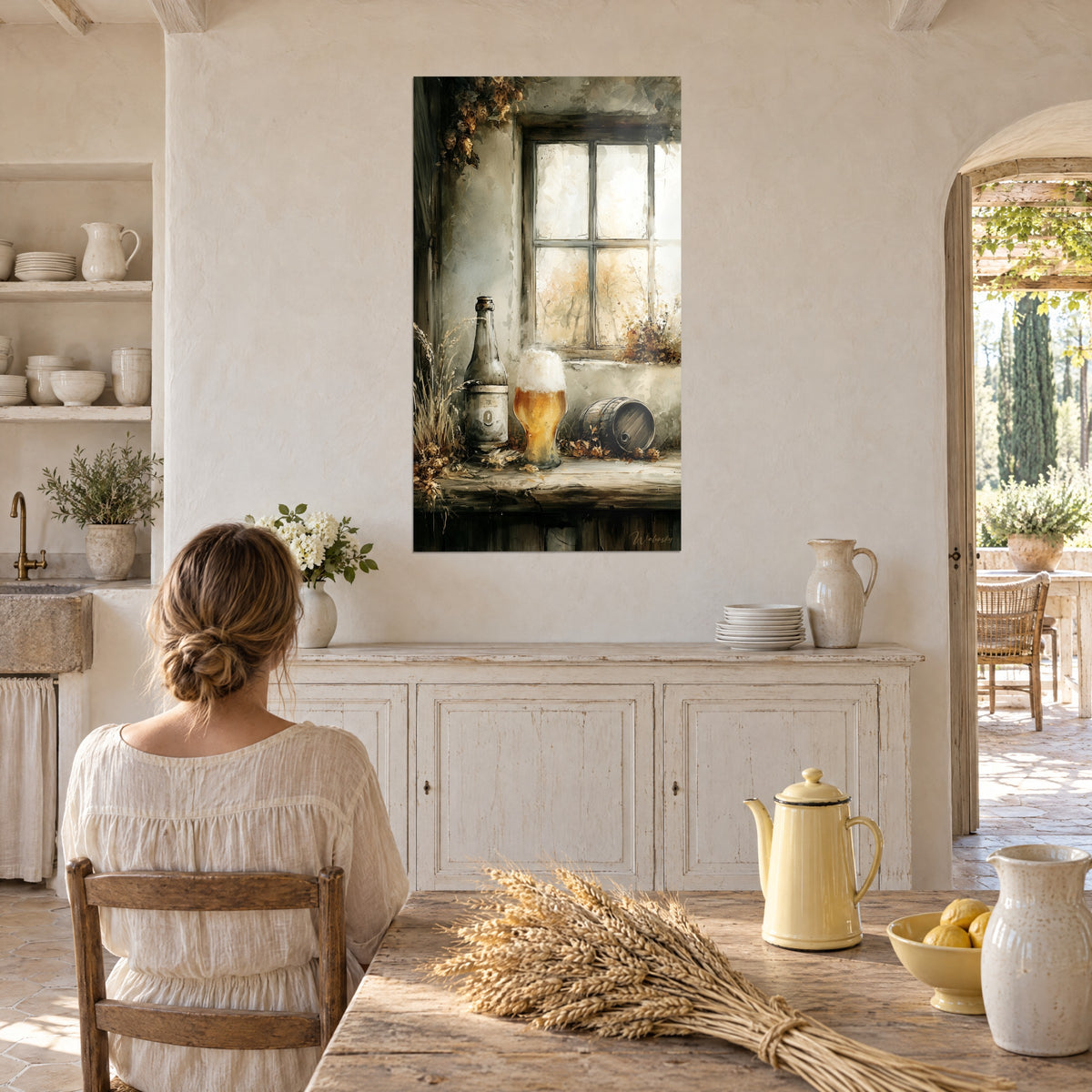 Schilderij amberkleurige pint met romig schuim, etiketfles, beige beslagen ruit, tegenover een vrouw met de rug naar de kijker in een keuken van een mas