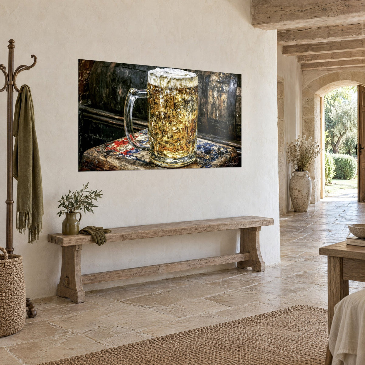 Tableau pinte ambrée coiffée de mousse crème, tonneaux sombres en fond, sur un mur beige près d'un banc en bois, maison en pierre
