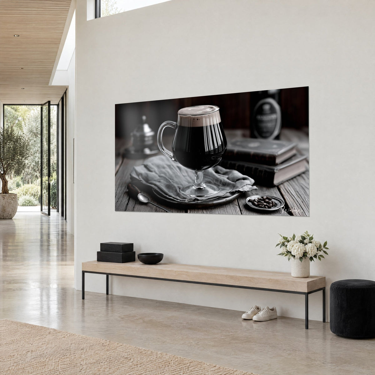 Tableau pinte noire à anse de verre, écume crémeuse et grains de café, vue de trois-quarts sur un mur blanc au-dessus d'un banc