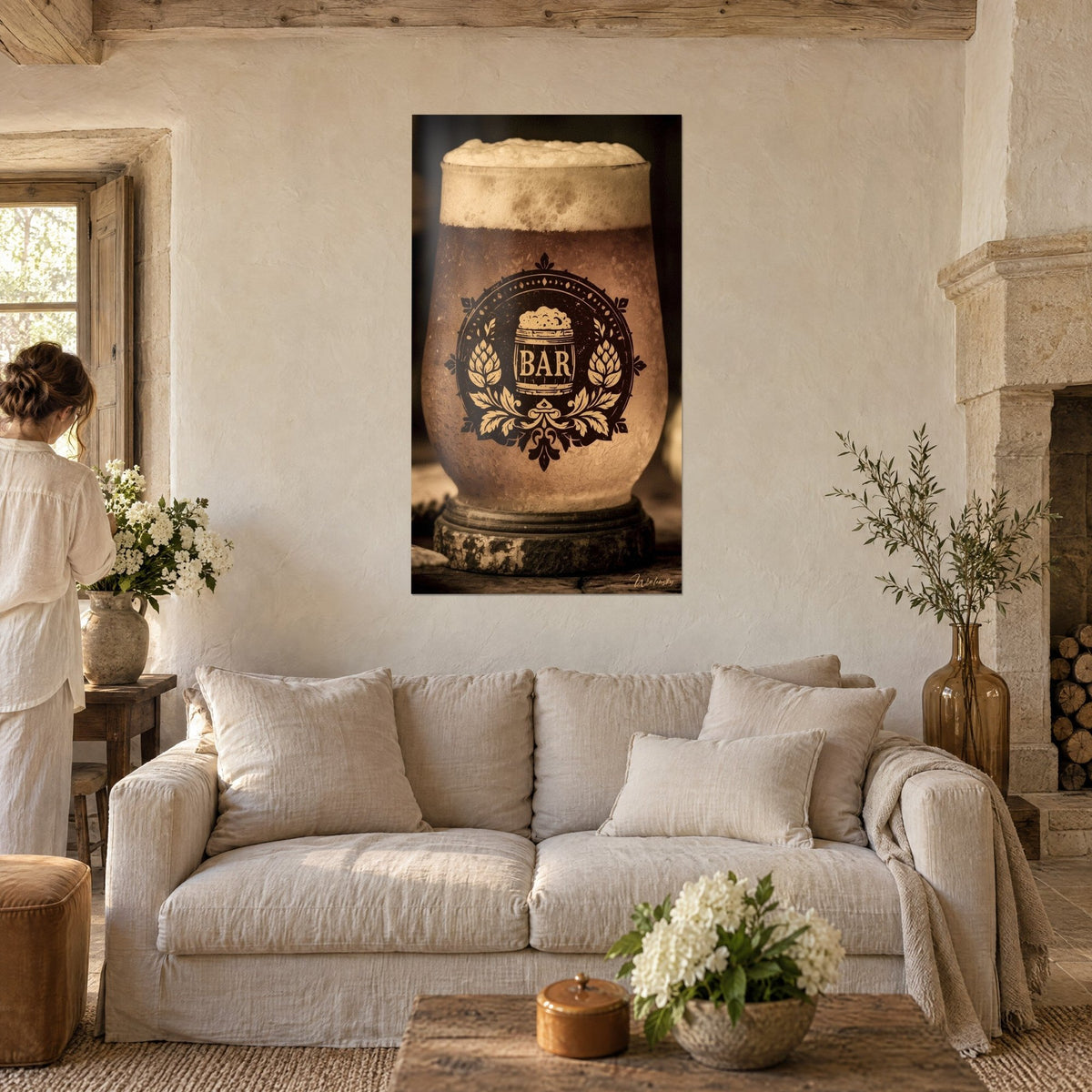 Quadro boccale di birra spumosa ambrata e stemma dorato, una donna di spalle, pareti bianche, sopra un divano in un soggiorno luminoso
