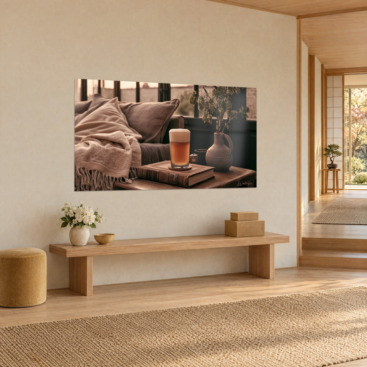 Wall art of a copper-blonde beer with creamy foam in a glass, beige fringed throw and green hop sprig, on a cream wall in three-quarter view