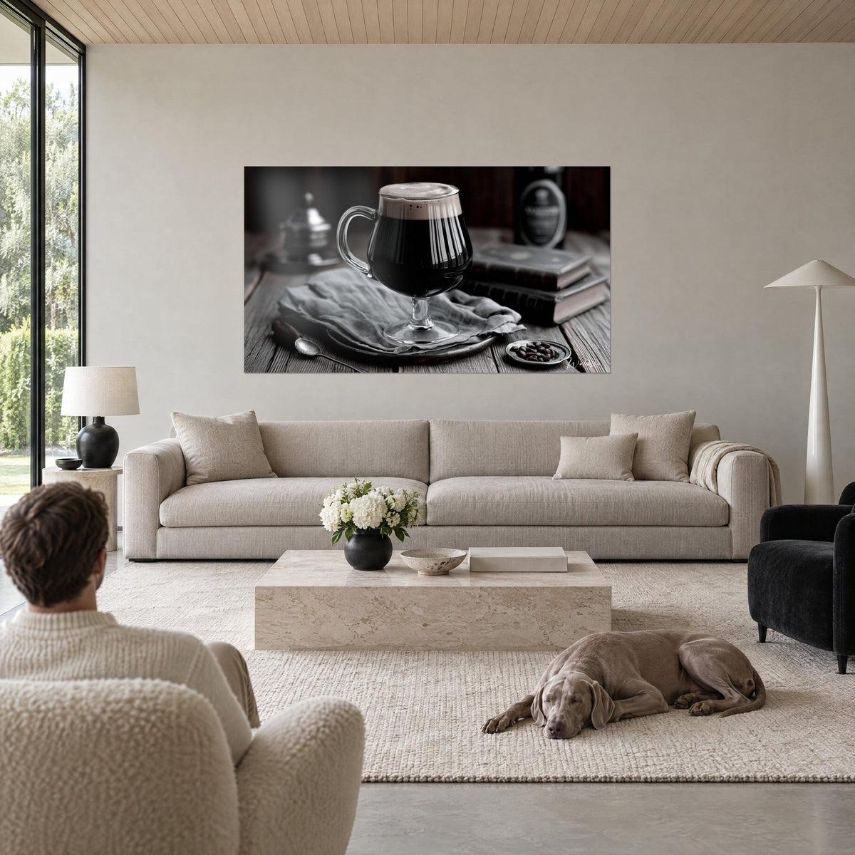 Tableau chope de bière brune coiffée de mousse beige, tissu gris et livres anciens, au-dessus d'un canapé dans un salon lumineux