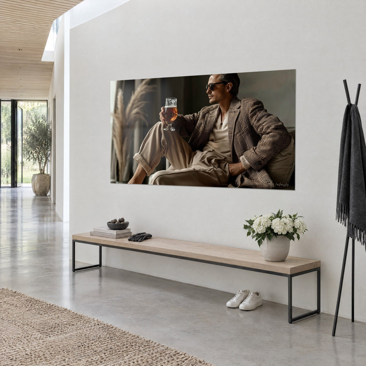 Tableau gentleman aux lunettes noires assis en veston à carreaux brun, verre de bière cuivrée, pampa beige, mur blanc d'une maison d'architecte