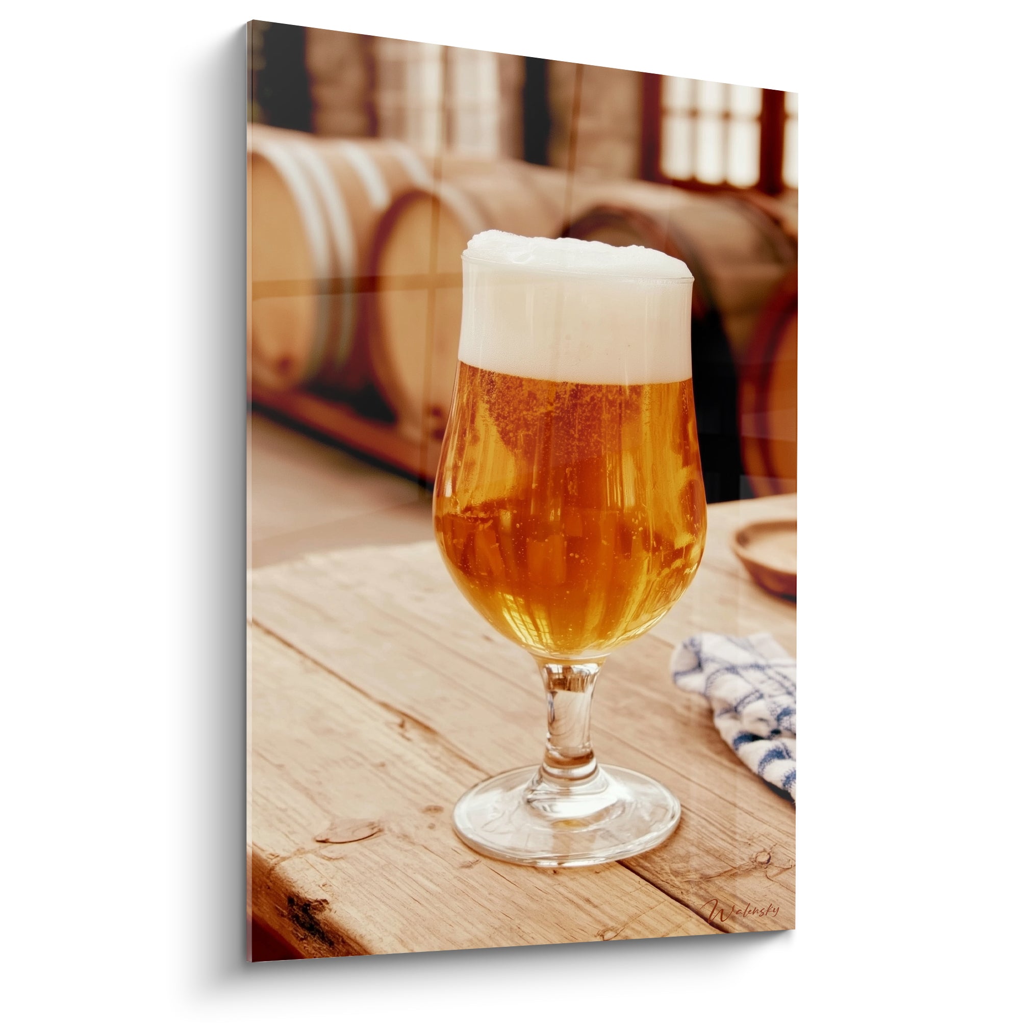 Verre à pied de bière ambrée et mousse blanche sur table en bois clair devant des fûts bruns