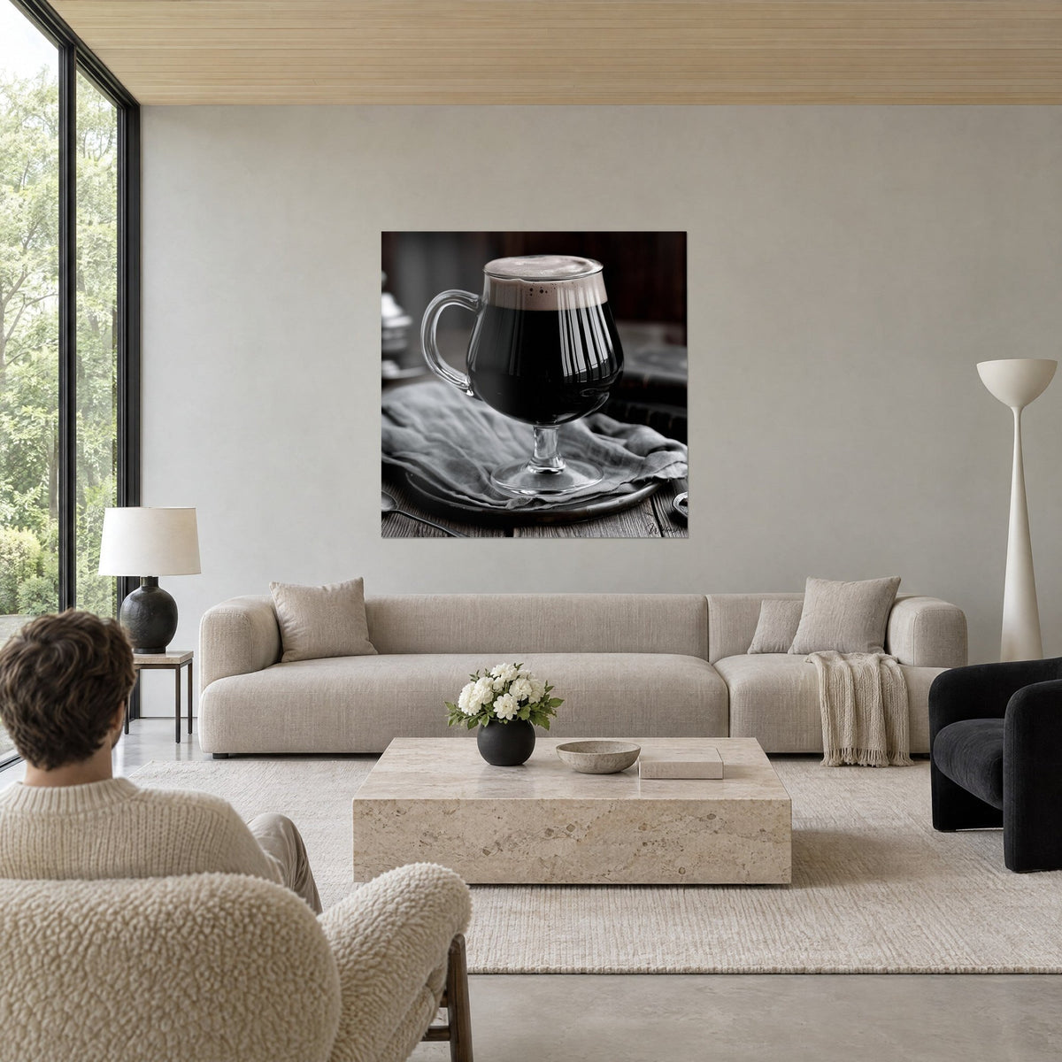 Schilderij van een bierglas op voet van transparant glas, zwart bier met beige schuim, verfrommeld grijs tafelkleed, boven een bank in een lichte woonkamer