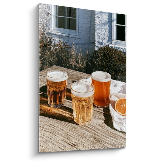 Trois verres de bière ambrée et dorée sur table en bois, lumière rasante et façade grise
