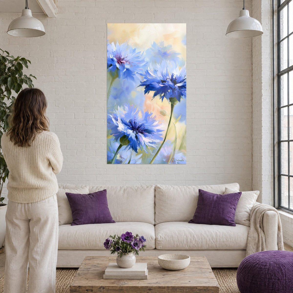Wall art of frayed azure cornflower petals on a peach background, a woman seen from behind, above a sofa in a bright living room