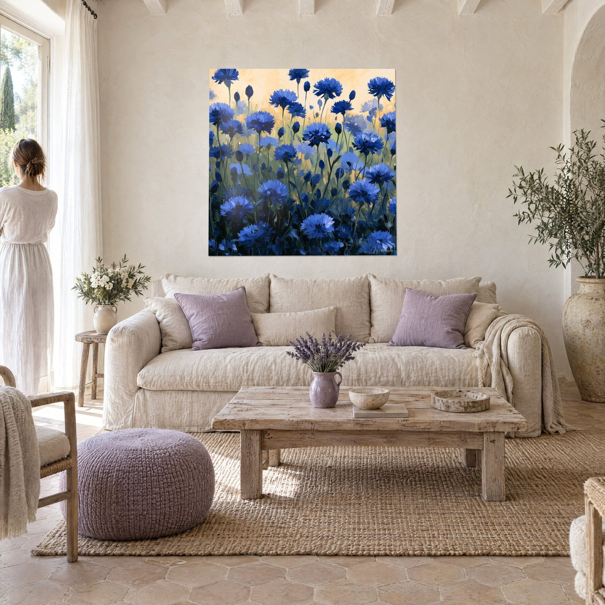 Tableau champ de bleuets peint à l'huile, fleurs bleu cobalt sur fond pêche, femme de dos au-dessus d'un canapé dans un salon lumineux