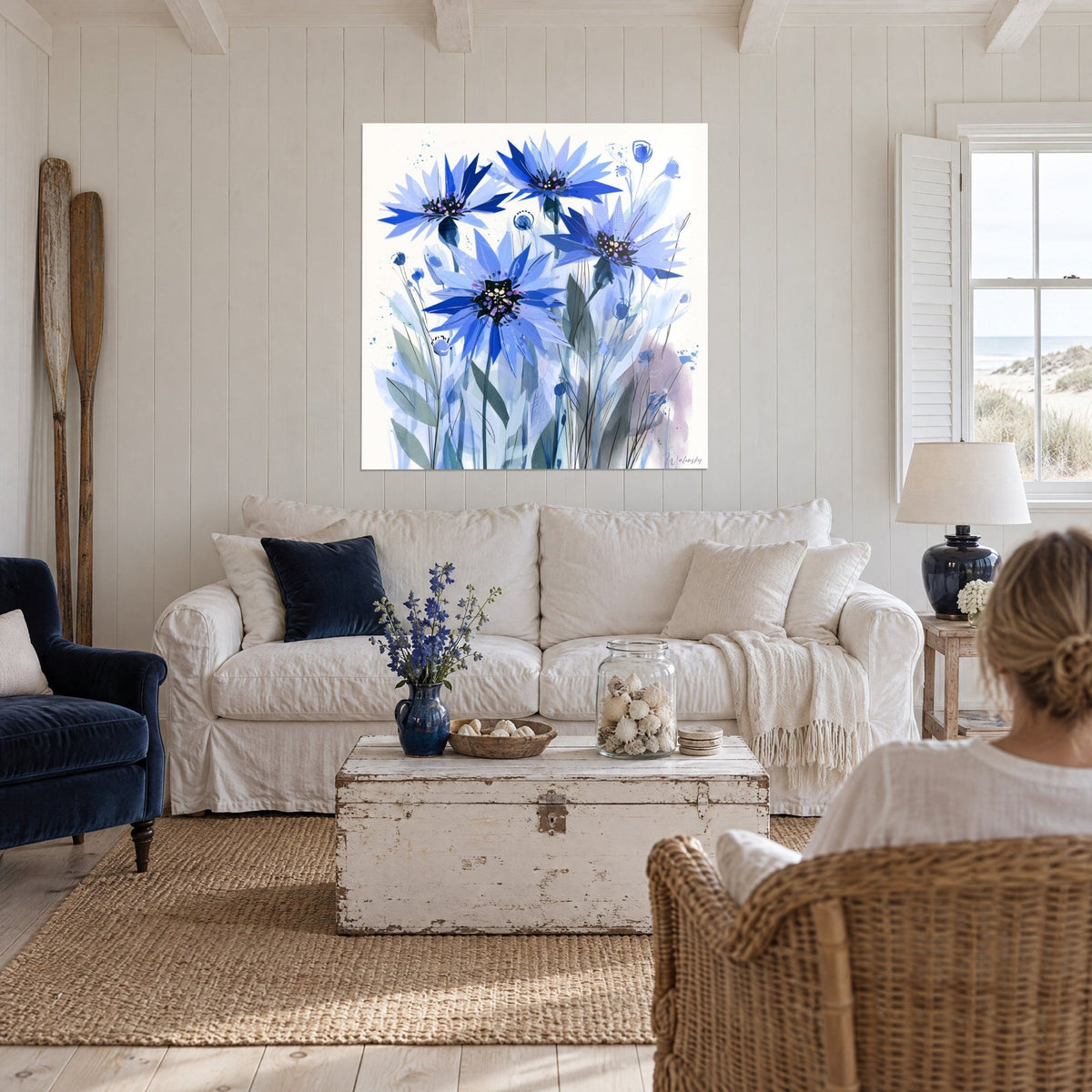 Schilderij korenbloemen van uitgesneden papier in kobaltblauw en lavendel, gespikkelde zwarte hartjes, boven een bank in een lichte woonkamer