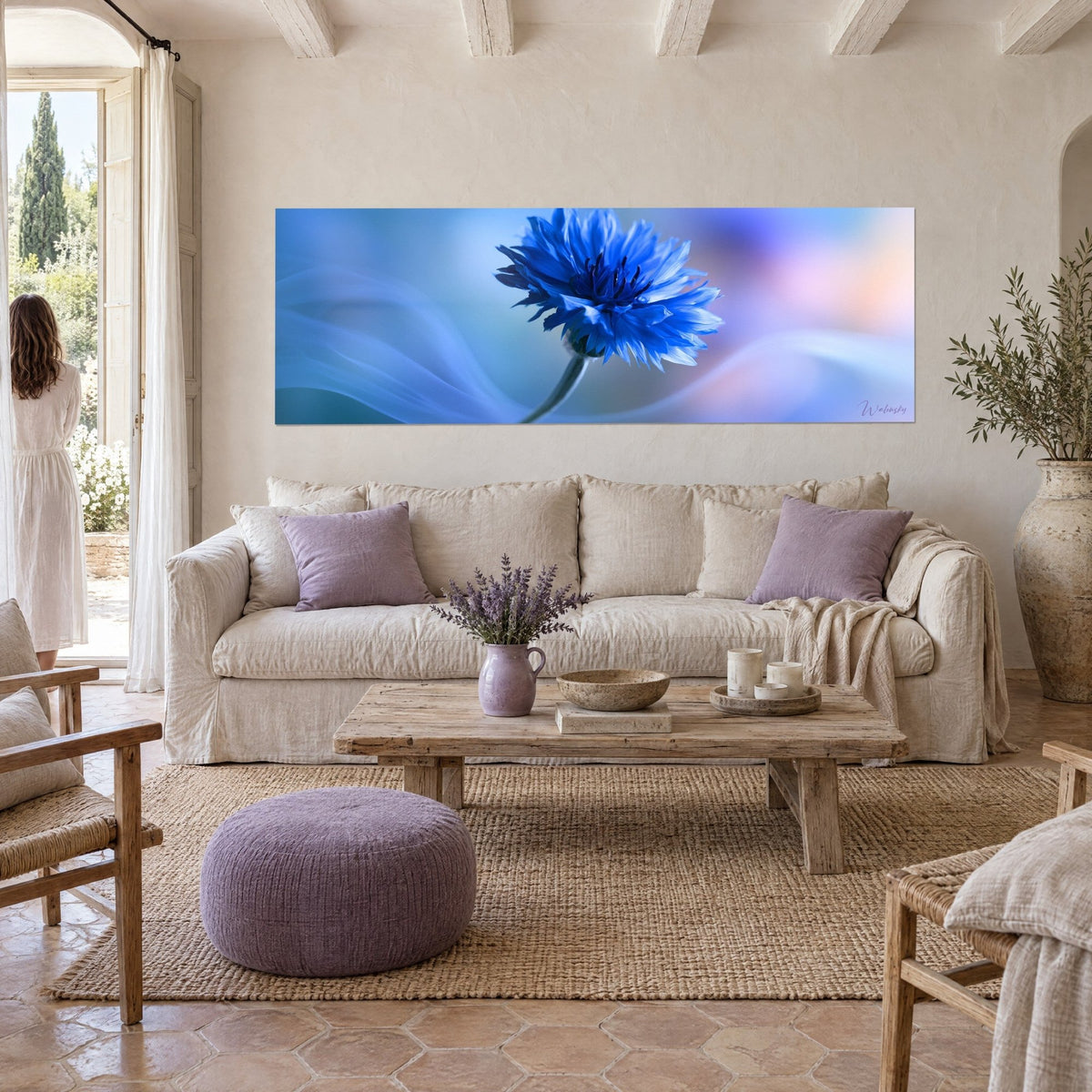Tableau bleuet aux pétales frangés bleu roi sur fond turquoise et rose pâle, au-dessus d'un canapé dans un salon lumineux