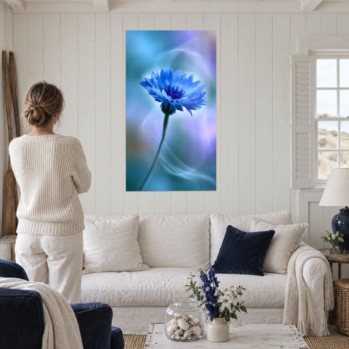 Tableau bleuet cobalt au cœur violet sur fond turquoise, volutes de fumée, femme de dos, au-dessus d'un canapé dans un salon lumineux