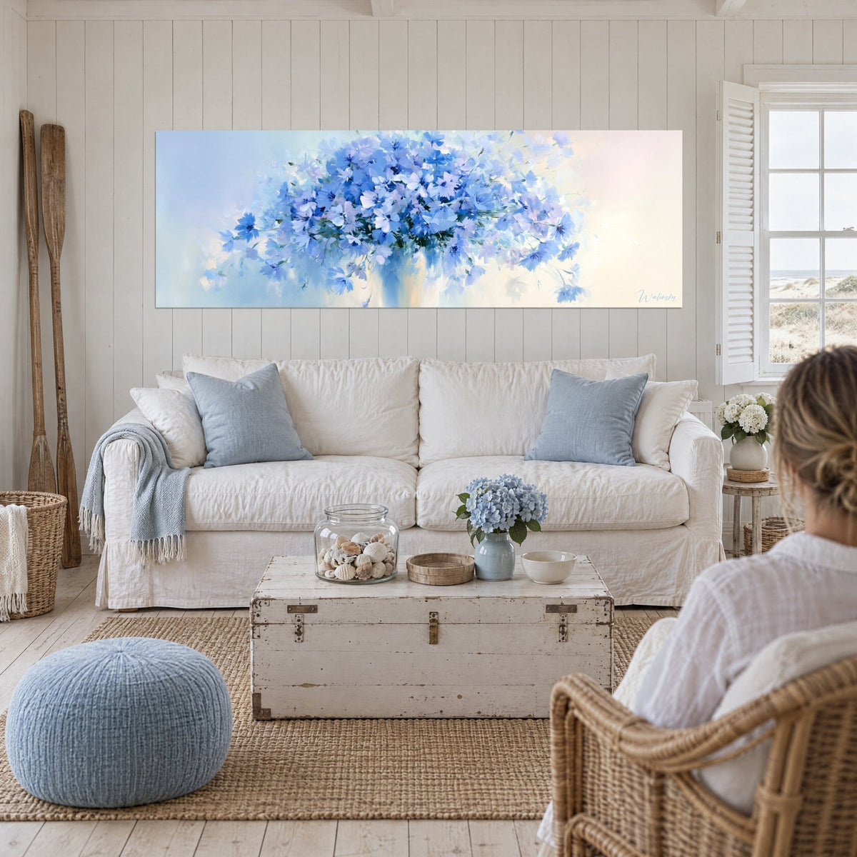 Tableau gerbe de bleuets azur et lilas dans un vase évasé, panoramique, au-dessus d'un canapé dans un salon lumineux