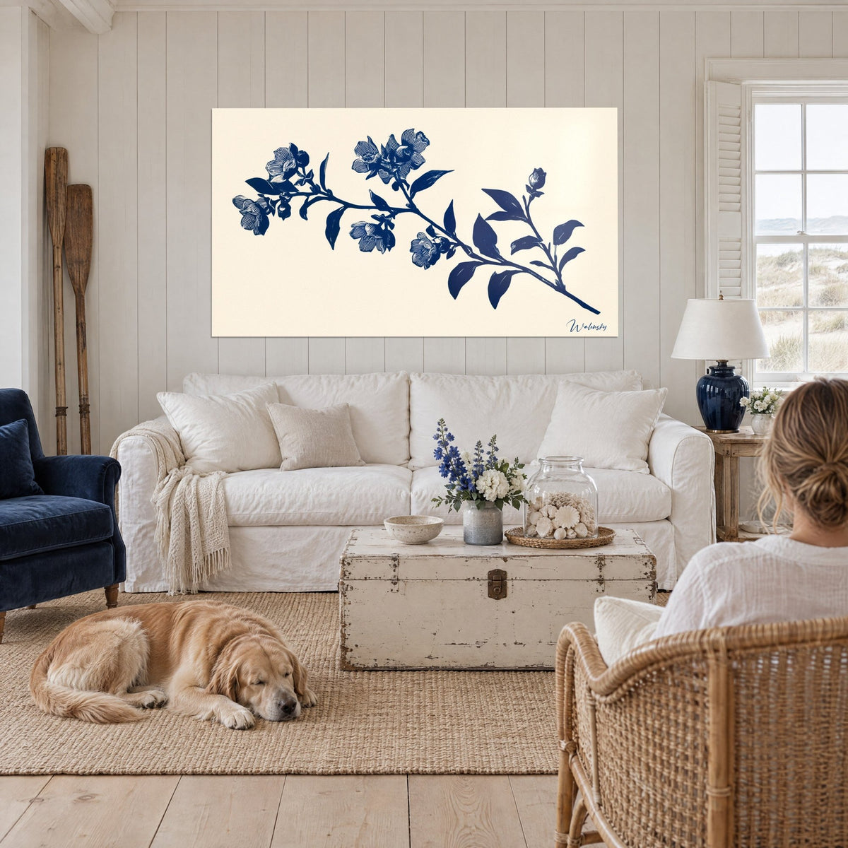 Tableau branche fleurie en linogravure bleu marine sur fond ivoire, un retriever couché, au-dessus d'un canapé dans un salon lumineux