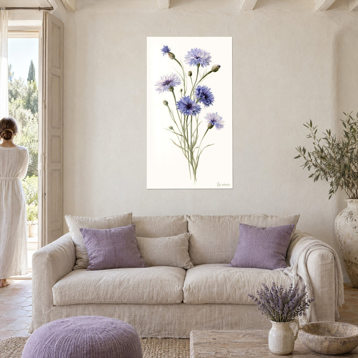Tableau bouquet de bleuets bleu-mauve aux tiges vert olive, fond ivoire, mur crépi, femme de dos au-dessus d'un canapé dans un salon lumineux