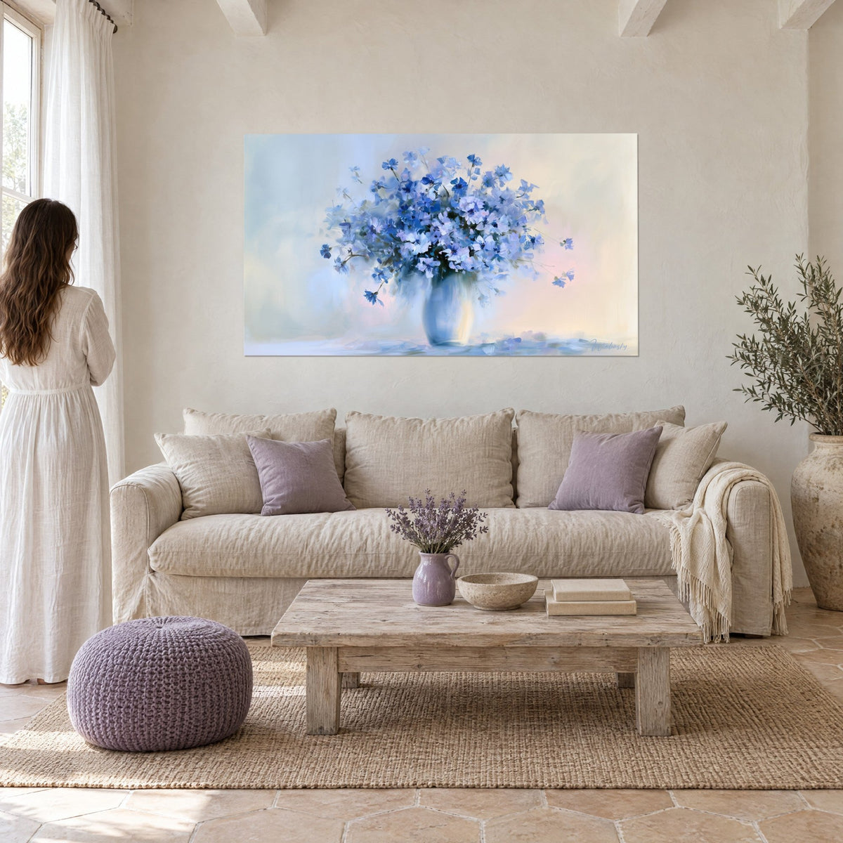 Tableau gerbe de bleuets bleu cobalt et lavande dans un vase pâle, fond crème rosé, femme de dos, au-dessus d'un canapé dans un salon lumineux