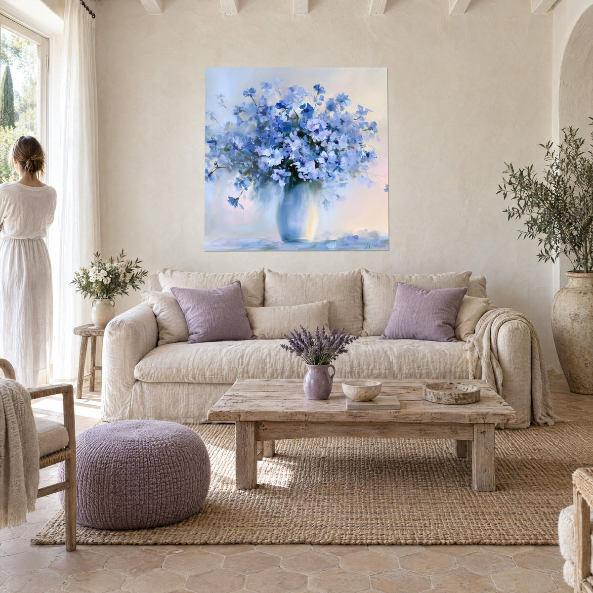 Tableau gerbe de bleuets aux pétales bleu outremer et lavande dans un vase pâle, fond rose poudré, au-dessus d'un canapé dans un salon lumineux