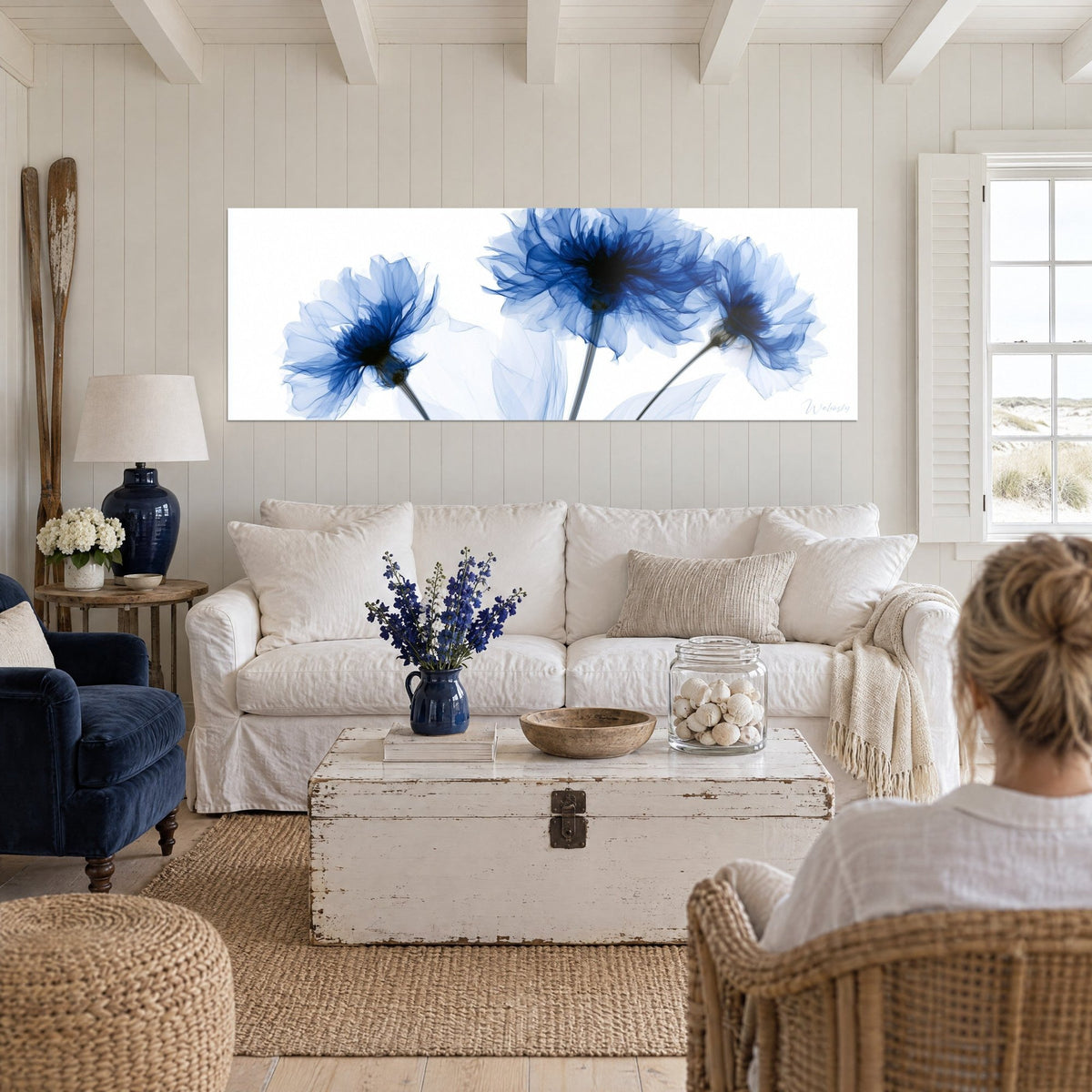 Tableau bleuets translucides en fleurs radiographiées, bleu marine et blanc, deux femmes de dos, au-dessus d'un canapé dans un salon lumineux