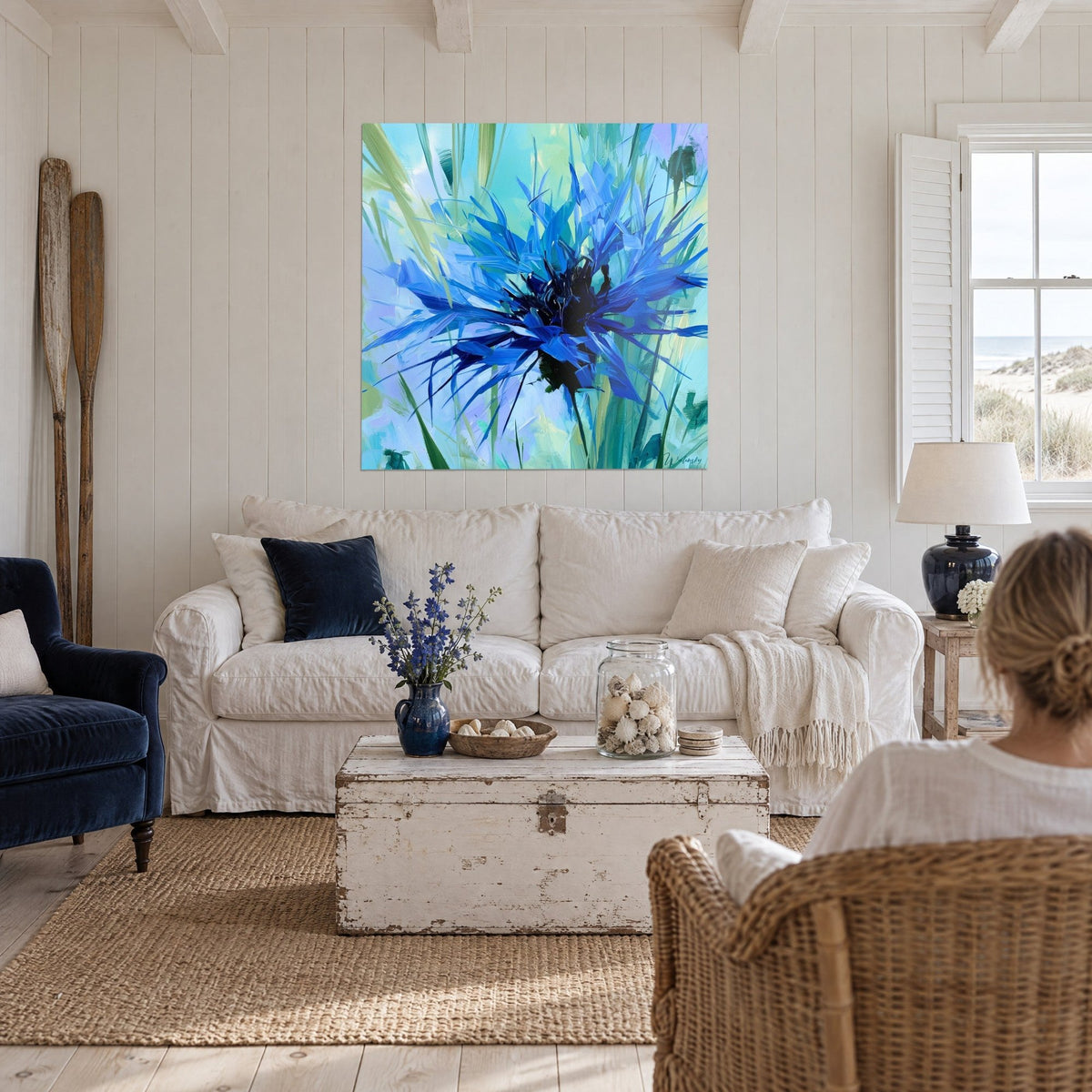 Tableau bleuet éclaté aux pétales bleu cobalt et turquoise, cœur noir, au-dessus d'un canapé dans un salon lumineux