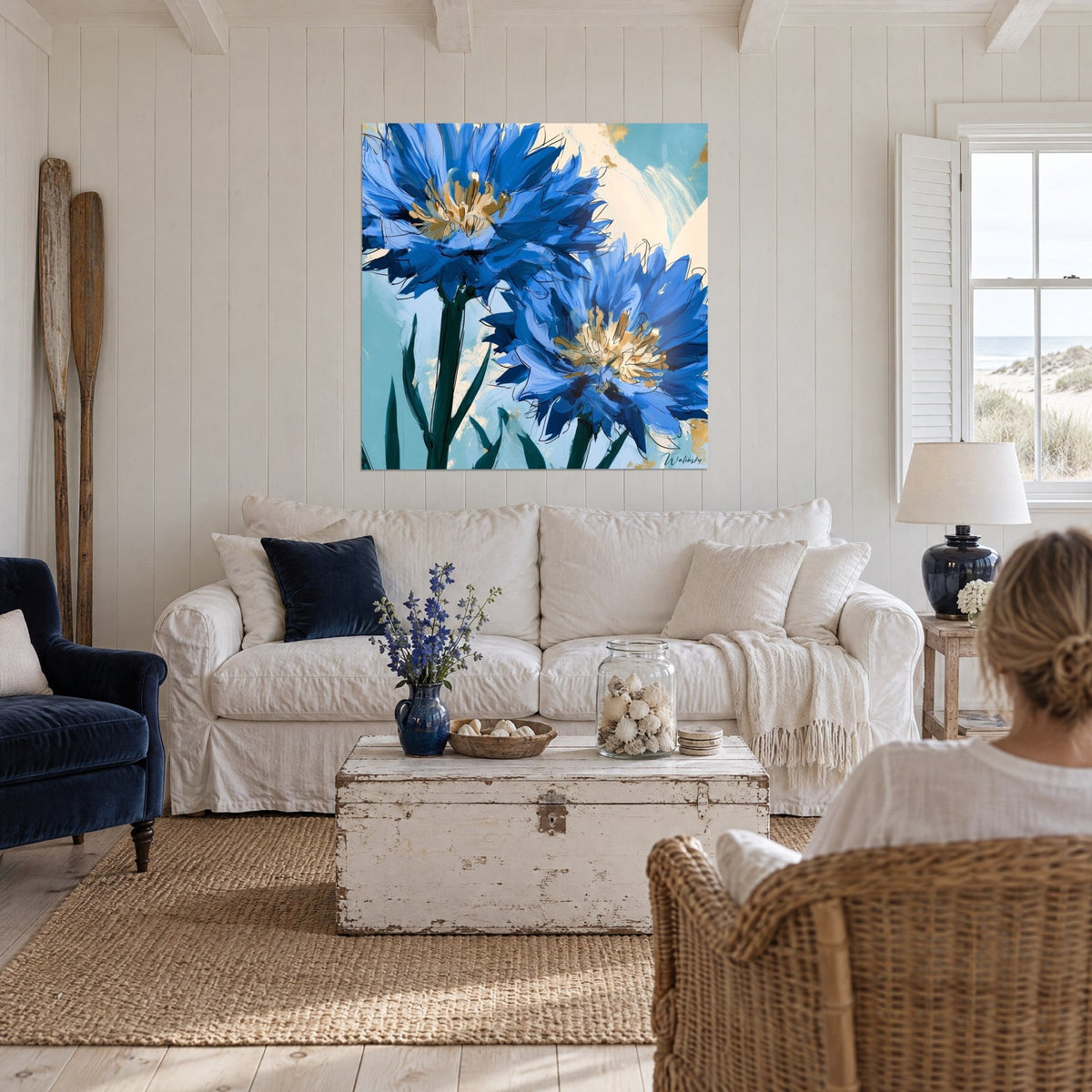 Tableau bleuets bleu cobalt aux cœurs dorés et tiges vert sapin, deux personnes de dos, au-dessus d'un canapé dans un salon lumineux