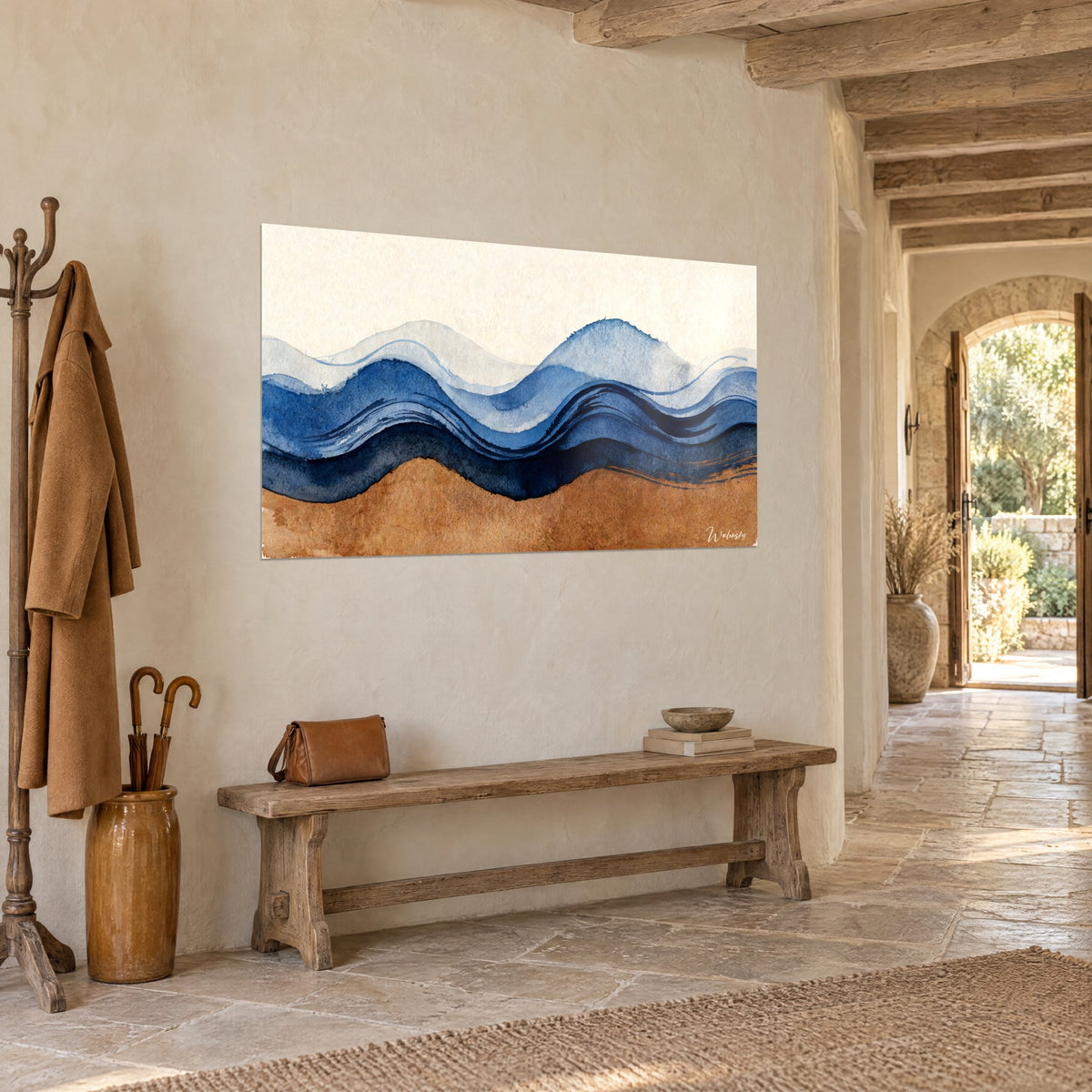 Tableau houle aquarellée indigo et sable doré accrochée dans une entrée en pierre, manteau camel et banc en bois