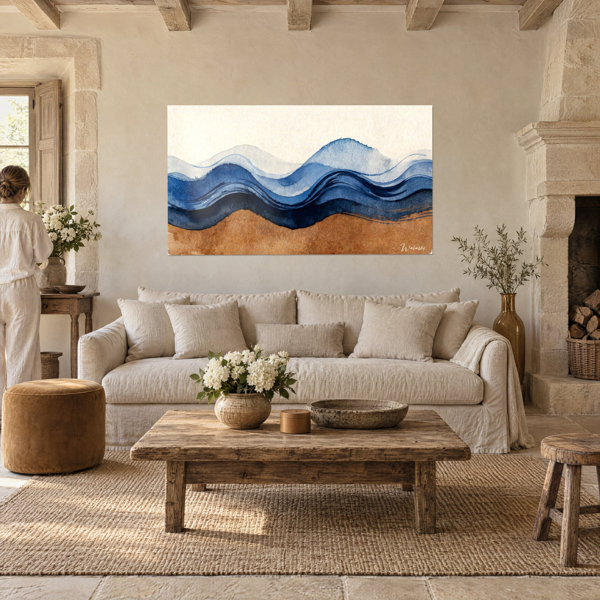 Tableau vagues ondulantes bleu marine et ocre sablé, fond crème, femme de dos, au-dessus d'un canapé dans un salon lumineux