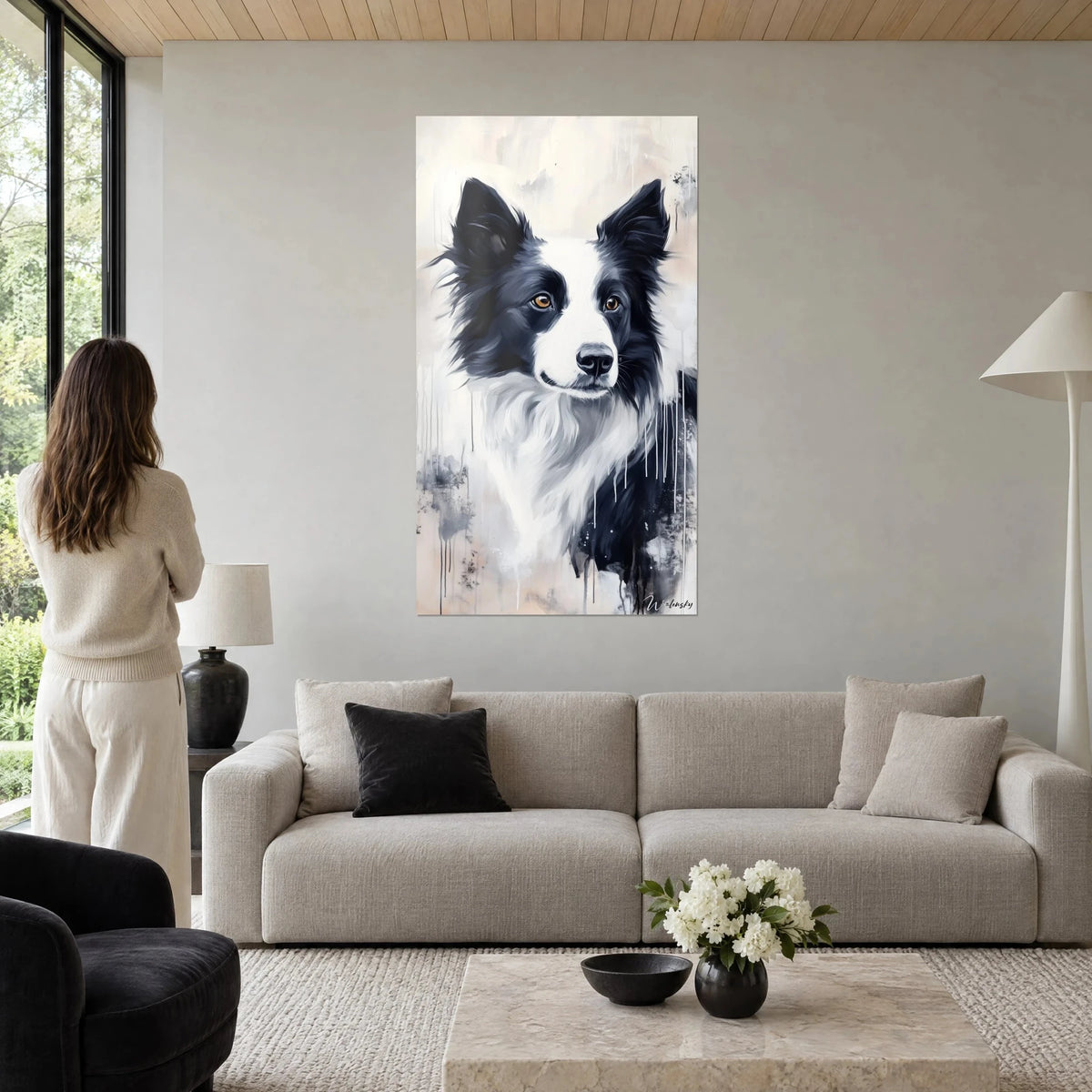 Obraz border collie czarno-biały o bursztynowych oczach, płynące beżowe tło, kobieta tyłem, nad sofą w jasnym salonie