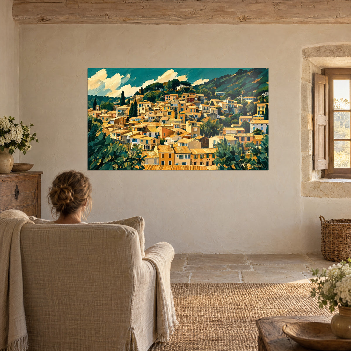 Tableau panorama de ruelles ocre et collines émeraude, une femme de dos dans un fauteuil en lin, fenêtre de pierre et vase de fleurs blanches