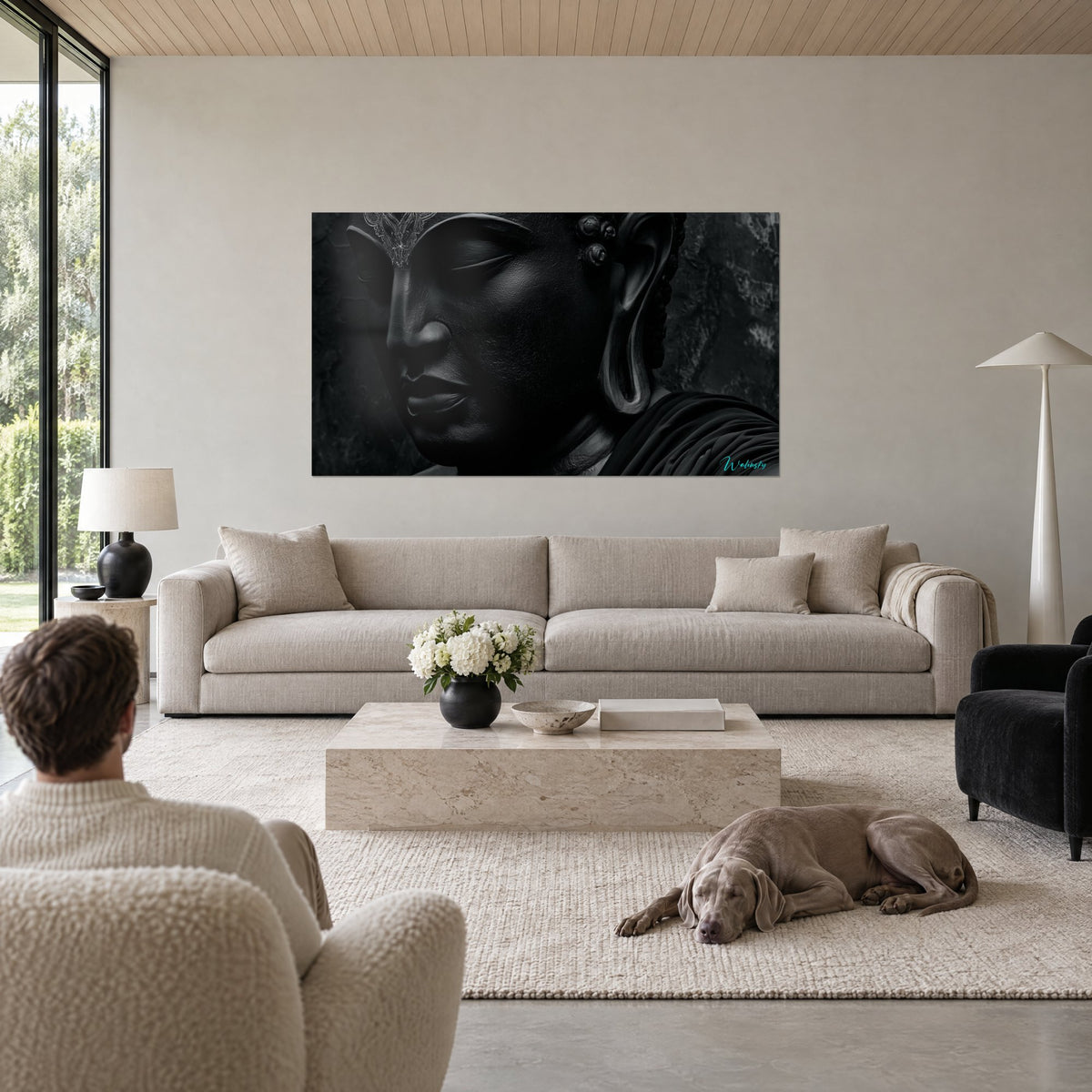 Tableau visage de Bouddha sculpté noir aux reflets anthracite, front ciselé d'argent, au-dessus d'un canapé dans un salon lumineux
