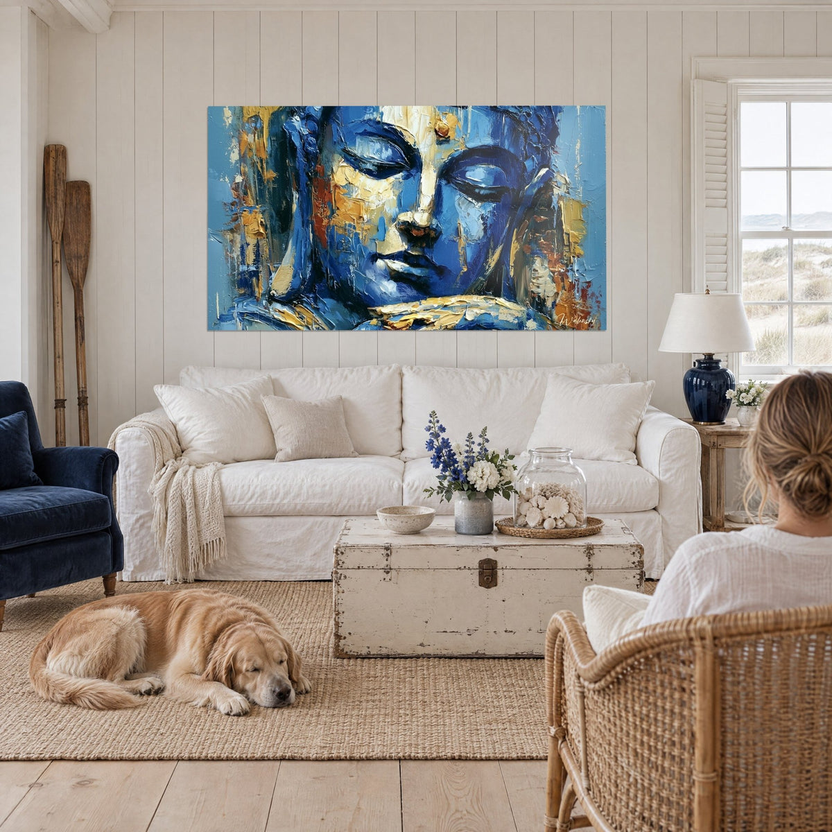 Tableau visage de Bouddha bleu cobalt aux paupières closes et touches dorées, au-dessus d'un canapé dans un salon lumineux
