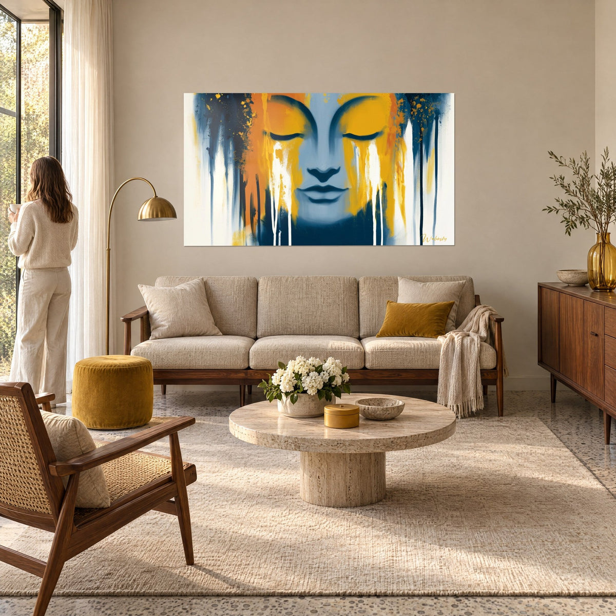 Cuadro rostro de Buda con párpados cerrados, chorreados ocre y azul marino, encima de un sofá en un salón luminoso