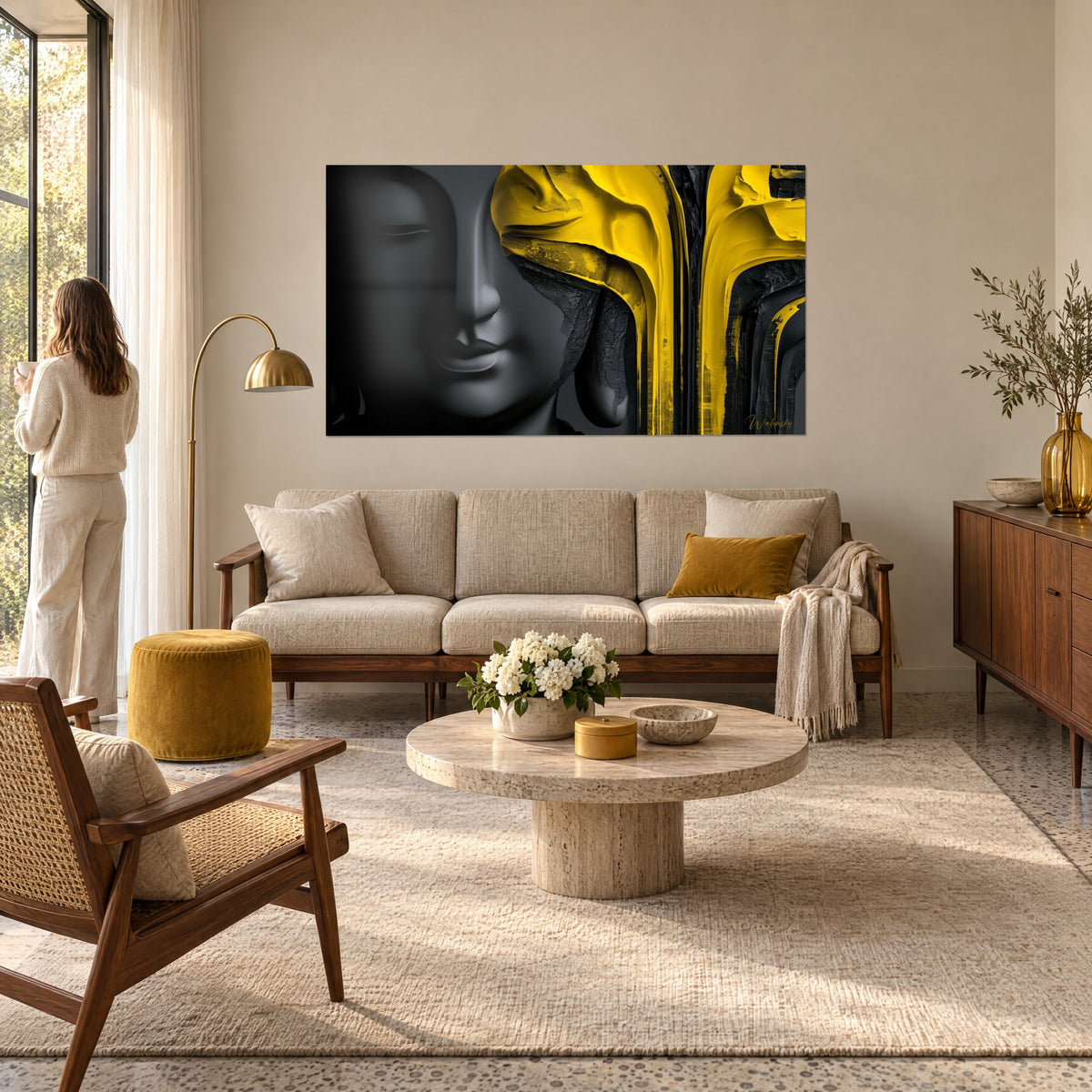 Tableau visage de Bouddha gris anthracite aux coulures jaune moutarde épaisses, femme de dos au-dessus d'un canapé dans un salon lumineux