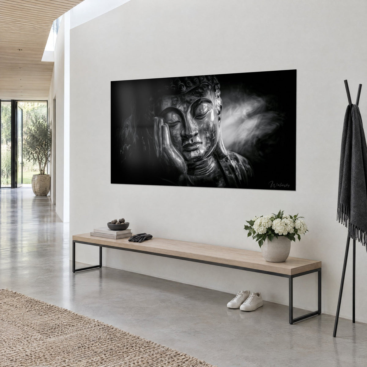 Tableau visage de Bouddha aux paupières closes, métal argenté et ombres noires, accroché de trois-quarts près d'un banc en bois clair