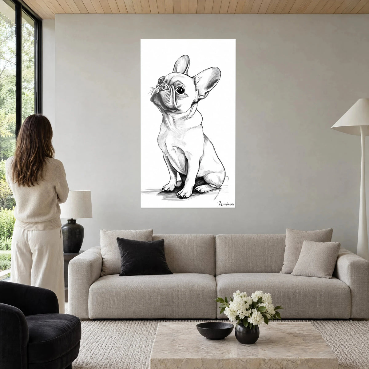 Wall art seated French bulldog, black and white, ears standing up, woman seen from behind, above a sofa in a bright living room