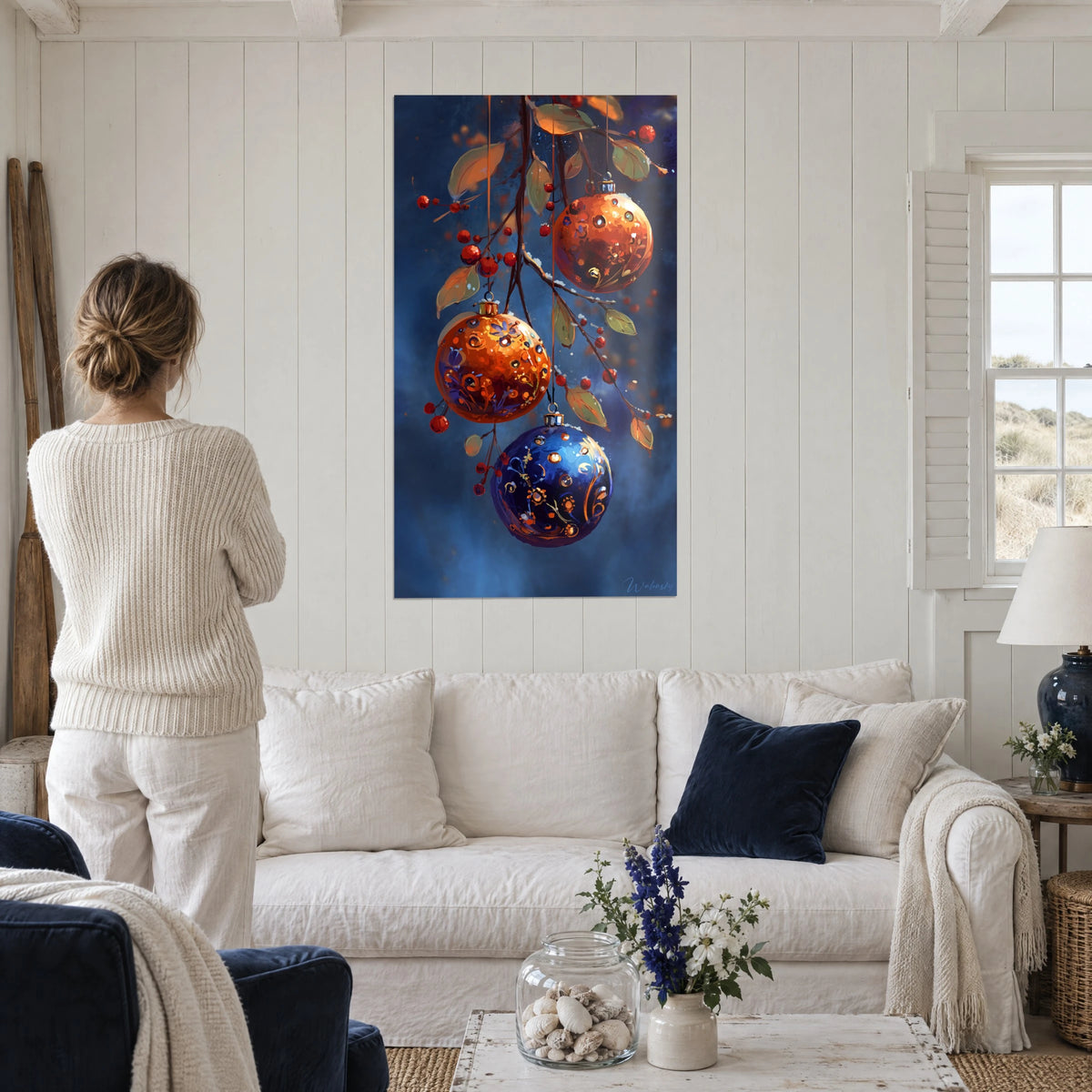 Cuadro de bolas de Navidad naranjas y azul medianoche colgadas de una rama de bayas rojas, encima de un sofá en un salón luminoso