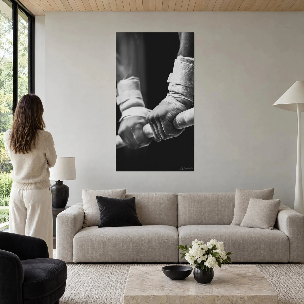 Tableau poings bandés de gaze blanche agrippant une barre sur fond noir, grisaille contrastée, au-dessus d'un canapé dans un salon lumineux