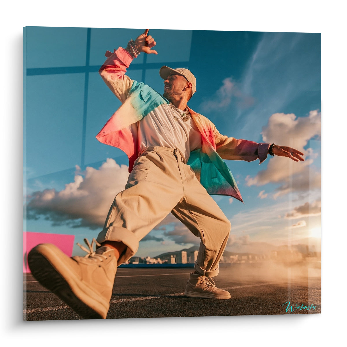 Danseur en pantalon beige et chemise corail turquoise, jambe tendue sous un ciel bleu éclatant